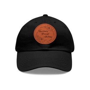 Könnte beinhalten: Eine schwarze Baseballkappe mit einem braunen Lederpatch, auf dem "Vasectomies Prevent Abortions" steht, umgeben von floralen Designs.