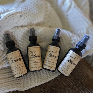 May include: Four black spray bottles with labels reading "A Thousand Dreams", "Spa Retreat", "Coastal Breeze", and "Heart & Home". Each bottle is labeled as a room and linen spray, 59 ml.