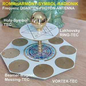 May include: A white hexagonal device with a gold sphere on top. The device has six circular plates with a gold pattern and a central circular plate with a blue and white pattern. The device is labeled "ROMMHARMONY-SYMBOL-RADIONIK", "Frequenz QUANTEN-PHOTON-ANTENNA", "Holy-Symbol TEC", "Lakhovsky RING-TEC", "Beamer-Magnet Messing-TEC", "VORTEX-TEC", "RESONANCE-ENERGY-DEVICE", and "COSMIC-ANTENNA SHAMBALLA".