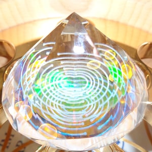 May include: A clear crystal pyramid with a white and green swirling pattern inside. The pyramid is sitting on a gold metal base.