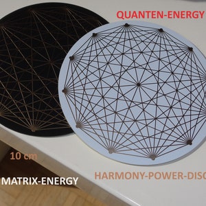 Puede incluir: Dos discos redondos, uno negro y otro blanco, con un patrón geométrico de líneas doradas y negras. Los discos tienen un diámetro de 10 cm y tienen el texto "QUANTEN-ENERGY" y "MATRIX-ENERGY" impreso en ellos. El disco blanco también tiene el texto "HARMONY-POWER-DISC" impreso en él.