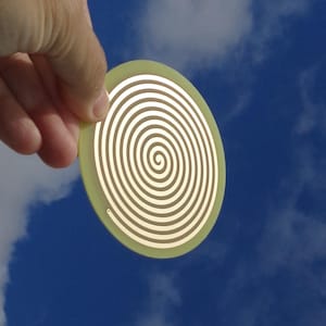 Puede incluir: Un disco redondo de color verde claro con un patrón en espiral en tonos marrones y blancos. El disco se sostiene en una mano contra un cielo azul con nubes blancas.