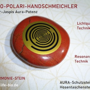 Puede incluir: Piedra de jaspe roja con un diseño circular dorado y negro. La piedra está etiquetada como "MWO-POLARI-HANDSCHMEICHLER" y "Roter-Jaspis Aura-Potenz".