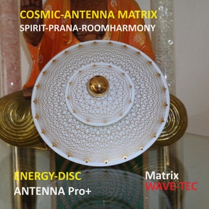Könnte beinhalten: Eine weiße kreisförmige Scheibe mit einem goldenen geometrischen Muster und einer goldenen Kugel in der Mitte. Die Scheibe ist mit "ENERGY-DISC ANTENNA Pro+" und "Matrix WAVE-TEC" beschriftet.