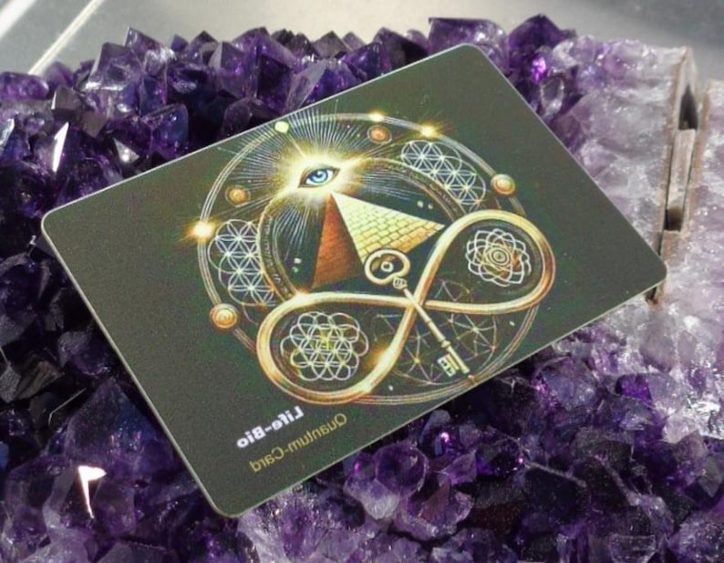 May include: A rectangular card with a detailed design featuring an eye, pyramid, key, and geometric patterns in gold and white on a dark background. The card is resting on a bed of purple amethyst crystals.