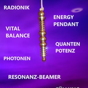 Puede incluir: Un péndulo de color dorado con una punta puntiaguda, colgando de una cuerda blanca. El péndulo está rodeado de texto en alemán, incluyendo "Aura", "Armonía", "Equilibrio vital", "Péndulo de energía", "Fotones", "Potencia cuántica", "Emisor de resonancia" y "Relleno de cristal cuántico".