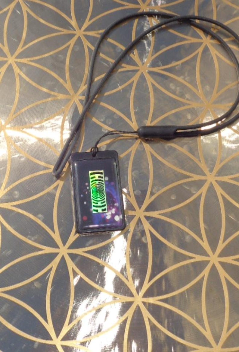 May include: A black pendant necklace with a rectangular pendant. The pendant features a colorful design with a green spiral and a cosmic background. The necklace has a black cord.
