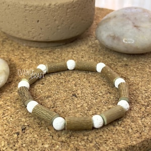 May include: A handmade bracelet featuring alternating wooden and white spherical beads. The wooden beads have a textured, bark-like appearance. The bracelet is displayed on a cork surface.