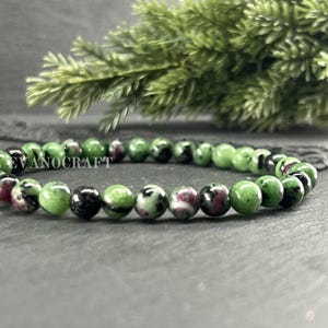 May include: A beaded bracelet featuring round, polished stones in shades of vibrant green, deep black, and magenta pink. The text EVANOCRAFT is visible on the left, and EVANOCRAFT JEWELRY CRAFTING is printed in the bottom right corner.