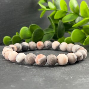 May include: A bracelet made of pink, grey, and white marbled stone beads.