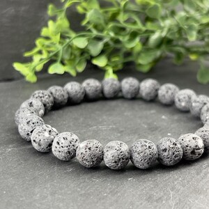 Peut inclure: Un bracelet en perles de roche volcanique grise. Les perles sont rondes et ont une surface rugueuse et texturée.