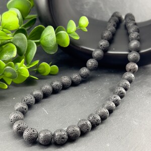 Peut inclure: Un collier de perles en pierre de lave noire. Les perles sont rondes et ont une surface rugueuse et texturée.