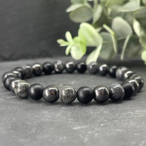 May include: A black and grey beaded bracelet with alternating round beads. The beads are made of black onyx and grey hematite.
