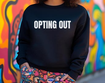 May include: A black sweatshirt with the text "OPTING OUT" printed in white on the front. The model is wearing the sweatshirt with colorful pants.