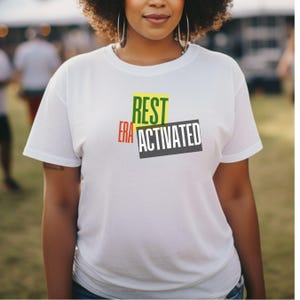 May include: White t-shirt with the words "REST ERA ACTIVATED" printed in green, yellow, red, and black.