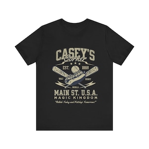 May include: Black t-shirt featuring the text "CASEY'S Corner" with baseball-themed graphics. The design includes crossed bats, a baseball, and the words "Main St. U.S.A. Magic Kingdom". The shirt also has the text "Relish Today and Ketchup Tomorrow!"