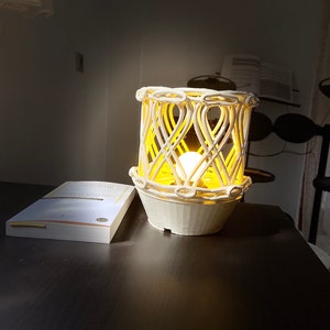 May include: A white ceramic lamp with a woven design and a warm yellow light. The lamp is sitting on a dark wooden table.