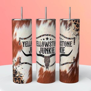 May include: Three stainless steel tumblers with lids and straws. The tumblers are wrapped in a cowhide pattern with a black and brown leopard print accent. The middle tumbler has the text "Yellowstone Junkie" with a star and a cow skull graphic.