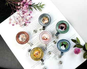 May include: Six colorful retractable badge holders with different animal pictures in the center. The holders are round and have a gold, silver, or blue frame. The animals include a cat, a dog, and a pug.