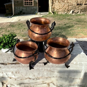 Peut inclure: Trois pots en cuivre avec des poignées et des pieds en fer noir. Les pots sont de tailles différentes et sont disposés en forme de pyramide.