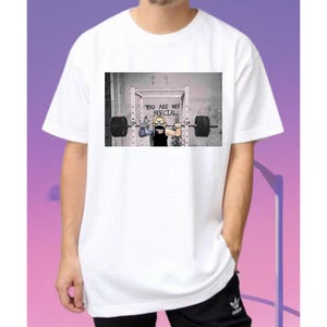 May include: White t-shirt with a graphic print of a cartoon character lifting weights. The text "You are not special" is written on the wall behind the character.