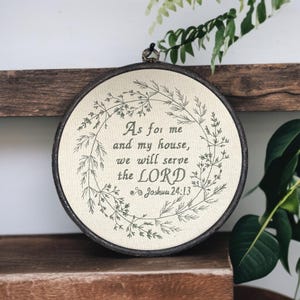 Peut inclure: Broderie circulaire encadrée avec la citation "As for me and my house, we will serve the LORD" entourée d'une couronne florale. Le texte et la couronne sont verts foncés, dans un cadre marron foncé.