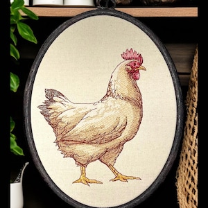 May include: Oval framed embroidery featuring a detailed hen illustration. The hen is depicted in shades of beige and brown with a red comb and yellow legs. The frame is dark with a metal loop for hanging. The background is a neutral canvas.