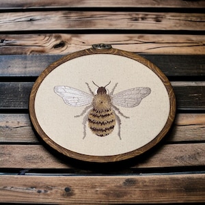 May include: Embroidered bee on a cream-colored canvas, framed in a dark wood hoop.
