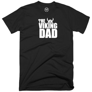 Könnte beinhalten: Schwarzes T-Shirt mit weißem Text, der "The Viking Dad" lautet. Der Text ist mit einem Wikingerhelm und einem Hammer gestaltet.