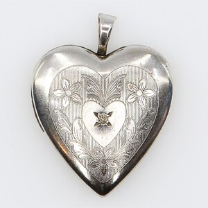 Peut inclure: Un pendentif médaillon en forme de cœur de couleur argentée avec un motif gravé de fleurs et de feuilles. Le centre du médaillon présente un cœur plus petit avec une petite pierre transparente à facettes au milieu. Une bélière est fixée au sommet.