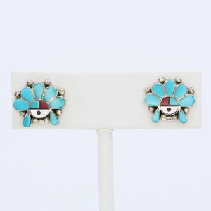 May include: A pair of silver earrings with turquoise and red stone inlays. The earrings are in the shape of a stylized flower with a circular design in the center.