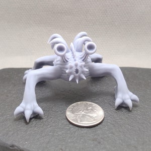 May include: A small, gray, 3D printed creature with multiple legs and a spiky body. It has two large, round eyes and a small, star-shaped mouth. The creature is about the size of a quarter.
