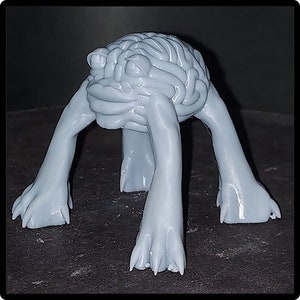 Op de afbeelding: Een grijs 3D-geprint beeldje van een brein met vier poten. De hersenen zijn getextureerd en de poten zijn glad.