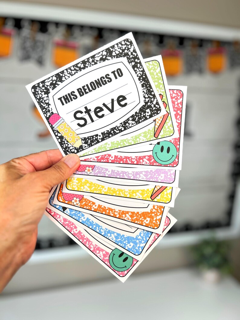 May include: A collection of colourful name tags with a notebook paper design. The top tag reads "THIS BELONGS TO Steve" with a pencil graphic. Other tags feature smiley faces and various patterns in pink, green, yellow, orange, and blue.
