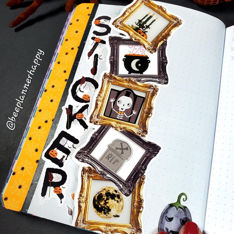 May include: A journal spread with Halloween-themed stickers. The word "STICKER" is spelled out vertically with individual letter stickers. Decorative stickers include framed images of a cauldron, skeleton, tombstone, and full moon. The journal has a yellow and black border.
