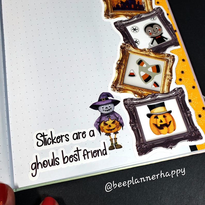 May include: A planner page with Halloween-themed stickers. The stickers include a vampire, candy corn, a jack-o'-lantern, and a scarecrow holding a pumpkin. Text on the page reads "Stickers are a ghouls best friend."
