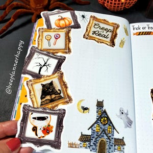 May include: A Halloween-themed journal spread featuring framed stickers of a pumpkin, lollipops, a bare tree, a black cat, and a mummy. Additional stickers include a haunted house, a ghost, and the phrase "Creep it Real".