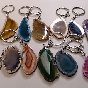 May include: Assortment of agate slice keyrings in various colours, including purple, blue, green, pink, and brown. Each slice is attached to a silver keyring.