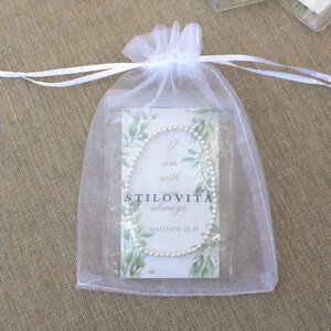 May include: A silver beaded bracelet inside a clear plastic bag, enclosed in a white organza drawstring bag. The card inside the bag reads "I am with you always. STILOVITA. Matthew 28:20" with a green leaf design.