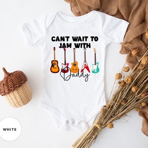 May include: White baby onesie with the text "Can't wait to jam with Daddy" and a row of five colorful guitars.