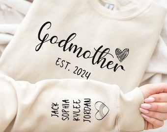May include: A cream-coloured sweatshirt featuring the word "Godmother" in a script font, with "EST. 2024" and a heart graphic. The sleeve shows names: Jack, Sophia, Kylee, Jordan, and a rainbow heart.