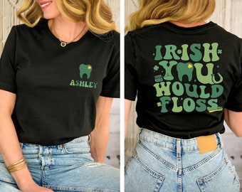 Może przedstawiać: Czarny T-shirt z zielonym nadrukiem zęba i tekstem "Ashley" z przodu. Z tyłu T-shirt ma zielony nadruk z tekstem "Irish You Would Floss" oraz wzory koniczyny, kapelusza leprechauna i podkowy.