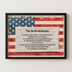 May include: A framed wall art piece featuring a distressed American flag background with a centred off-white fabric panel. The panel displays the text of The 1st Amendment in black, detailing rights regarding religion, speech, press, and assembly.