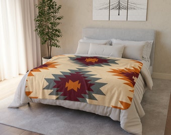 May include: A beige throw blanket with a geometric pattern in shades of orange, red, gray, and white. The blanket is folded on a bed with white pillows.