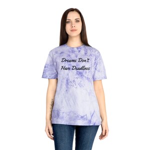 以下が含まれることがあります： 黒色の文字で「Dreams Don't Have Deadlines」と書かれた紫色のタイダイ染めTシャツです。