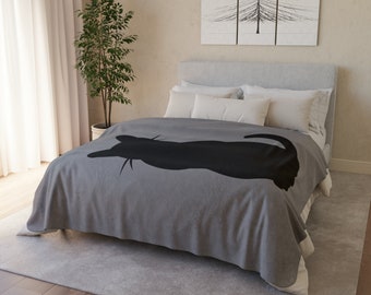 May include: A grey fleece throw blanket with a black silhouette of a cat curled up on it. The blanket is on a bed with white pillows and a grey headboard.