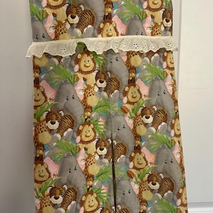 May include: A fabric baby changing station with a jungle animal print. The print features lions, tigers, elephants, and giraffes in a repeating pattern. The top edge has a cream-colored lace trim.