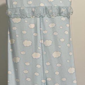 May include: A light blue diaper caddy with a white cloud pattern and a white lace trim. The caddy hangs from a hook.