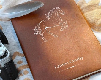 May include: A brown leather journal with a white horse illustration and the name "Lauren Crosby" embossed on the front.