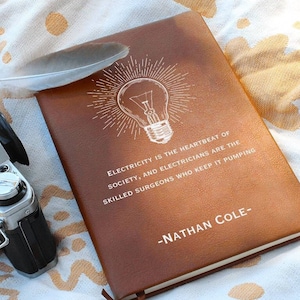 May include: A brown leather journal with a white lightbulb graphic and the quote "Electricity is the heartbeat of society, and electricians are the skilled surgeons who keep it pumping." -Nathan Cole-